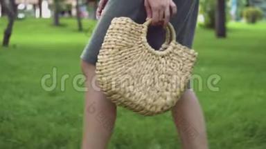 年轻的女人带着手工制作的时尚草包在夏季公园散步。 环保袋。